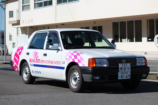 ピンクの市松模様とSUKUMOの文字が入った白い教習車