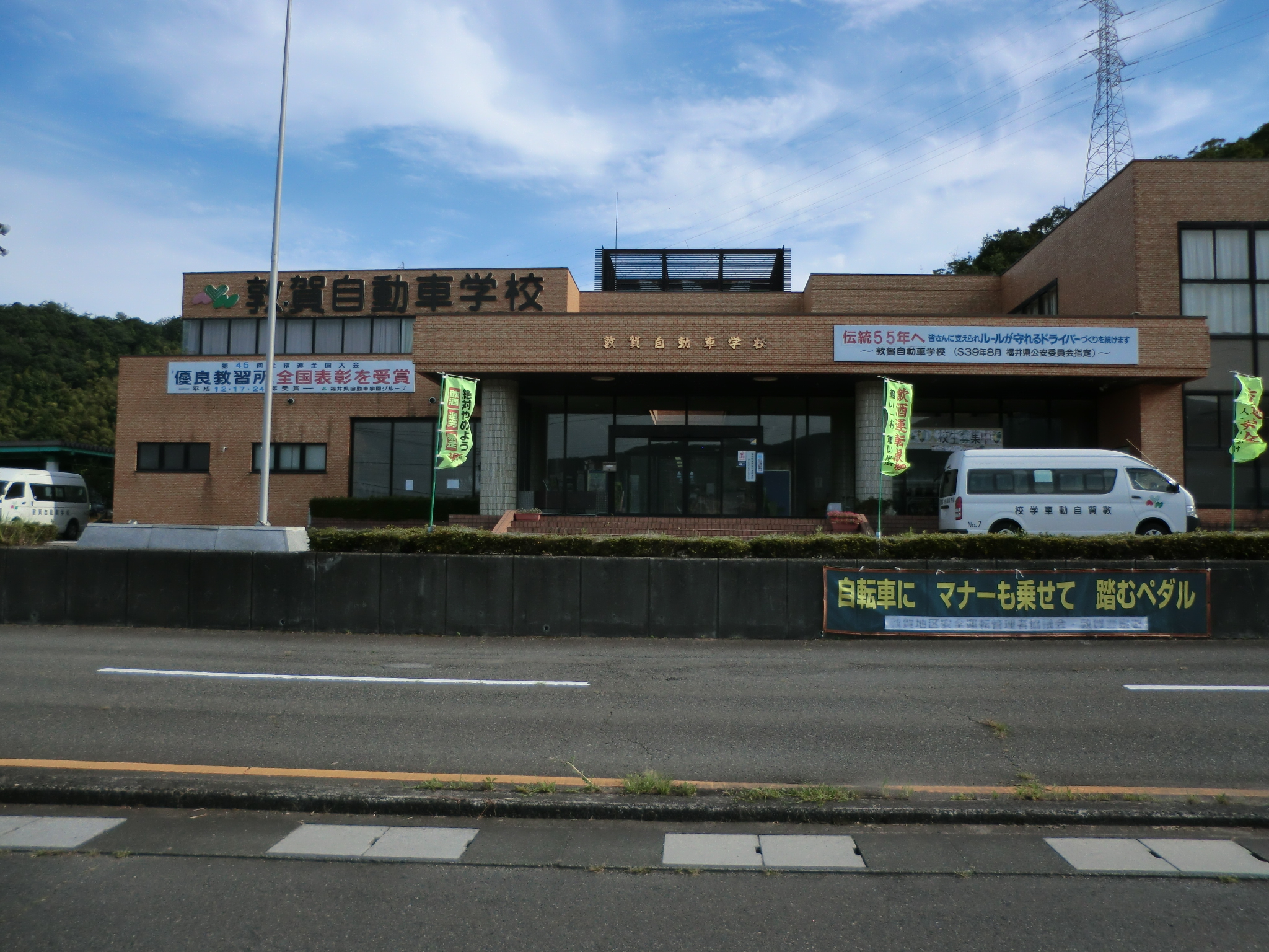 敦賀自動車学校の看板がかかった校舎の正面と送迎の車