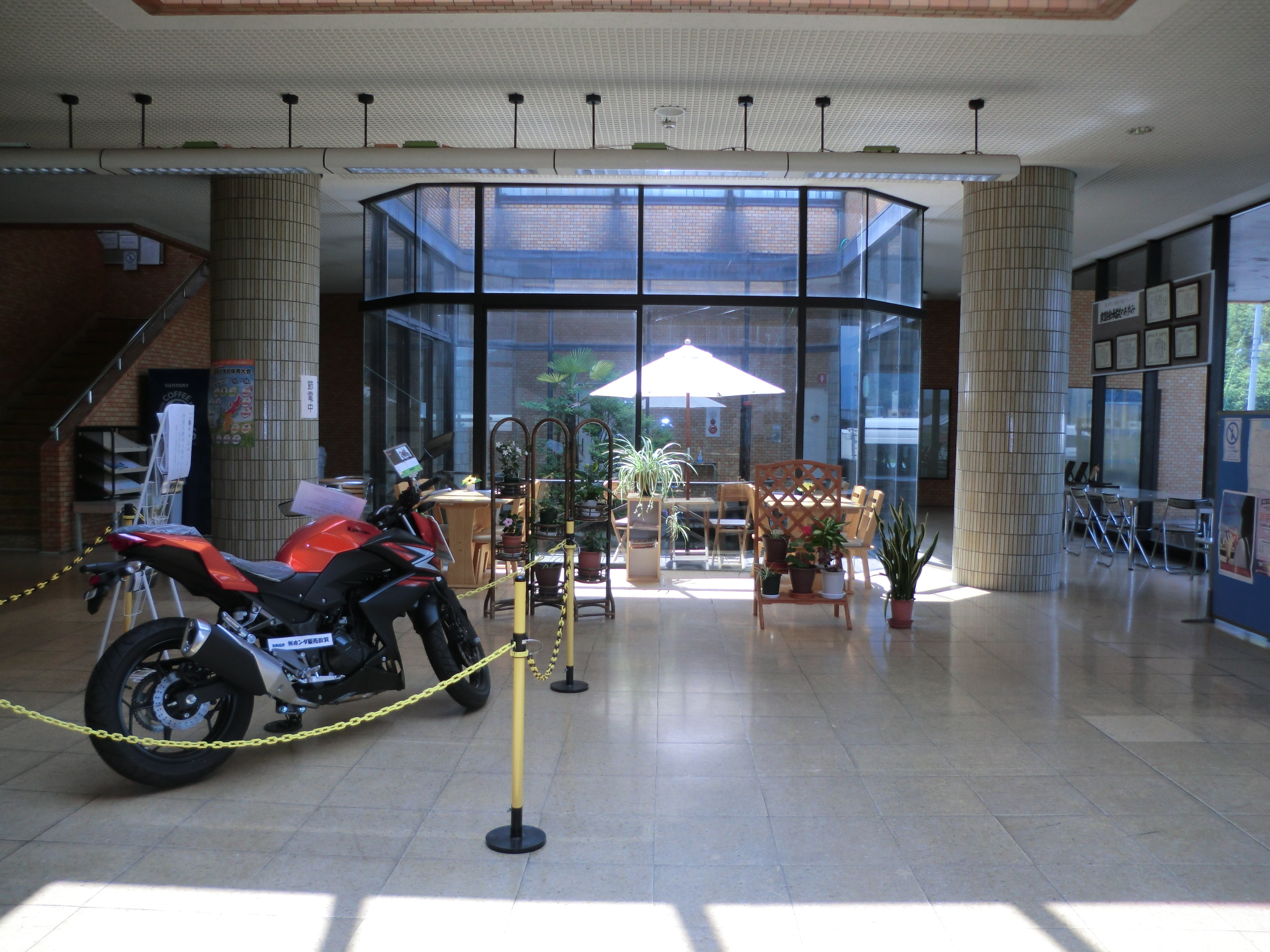 大きなガラス窓のある校舎のロビー。赤いバイクが展示されている